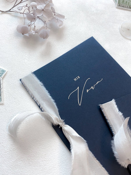 A set of two His and Her gold foil navy card stock vow books in calligraphy script with antique white colored silk ribbon