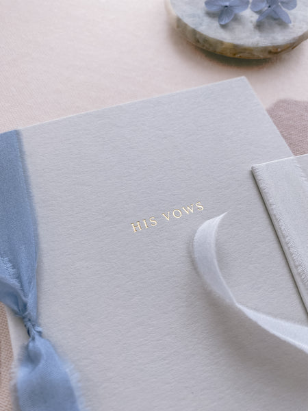 His gold foil gray card stock vow book in typeface font with blue colored silk ribbon