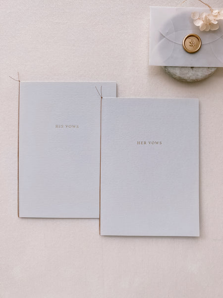 A set of two His and Her gold foil gray card stock vow books in typeface font with fine brown twine