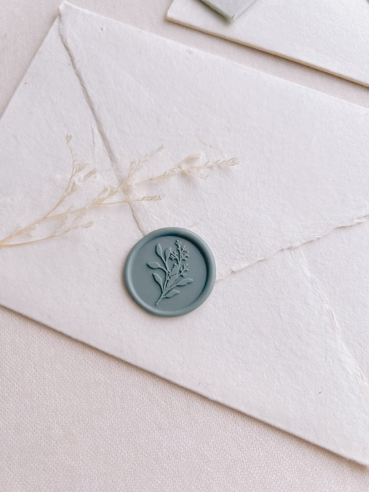 Dusty teal wax seal with a eucalyptus bouquet design, placed on a white envelope