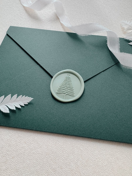 Pale sage green wax seal with delicate Christmas tree imprint on a dark green letter envelope
