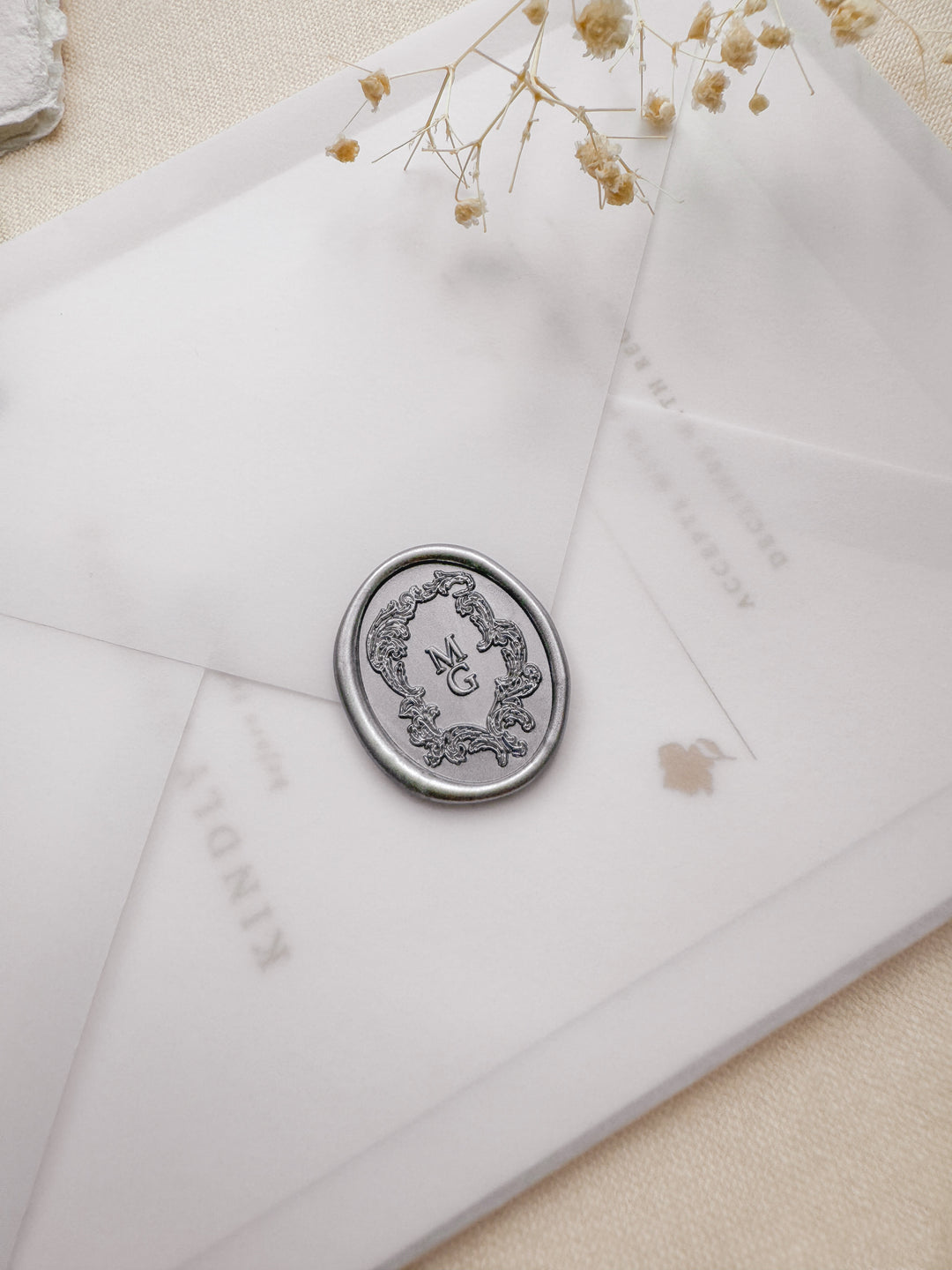 Silver personalized initials oval wax seal with a vintage crest monogram design, placed on a vellum envelope