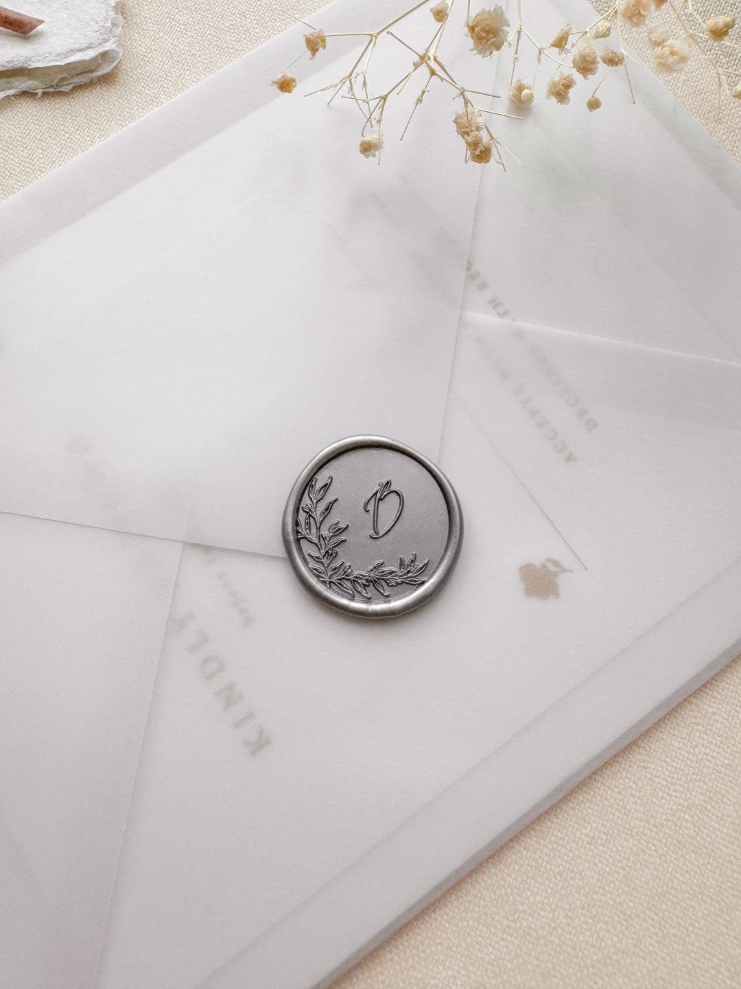 Silver personalized initials wax seal featuring a custom botanical monogram on a vellum wedding invitation envelope