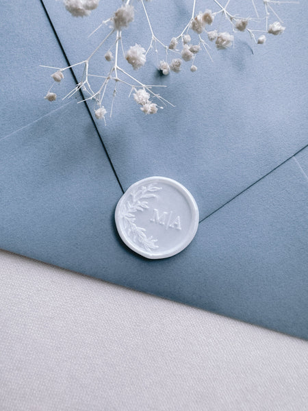 botanical design custom monogram pearl white wax seal on a dusty blue envelope 