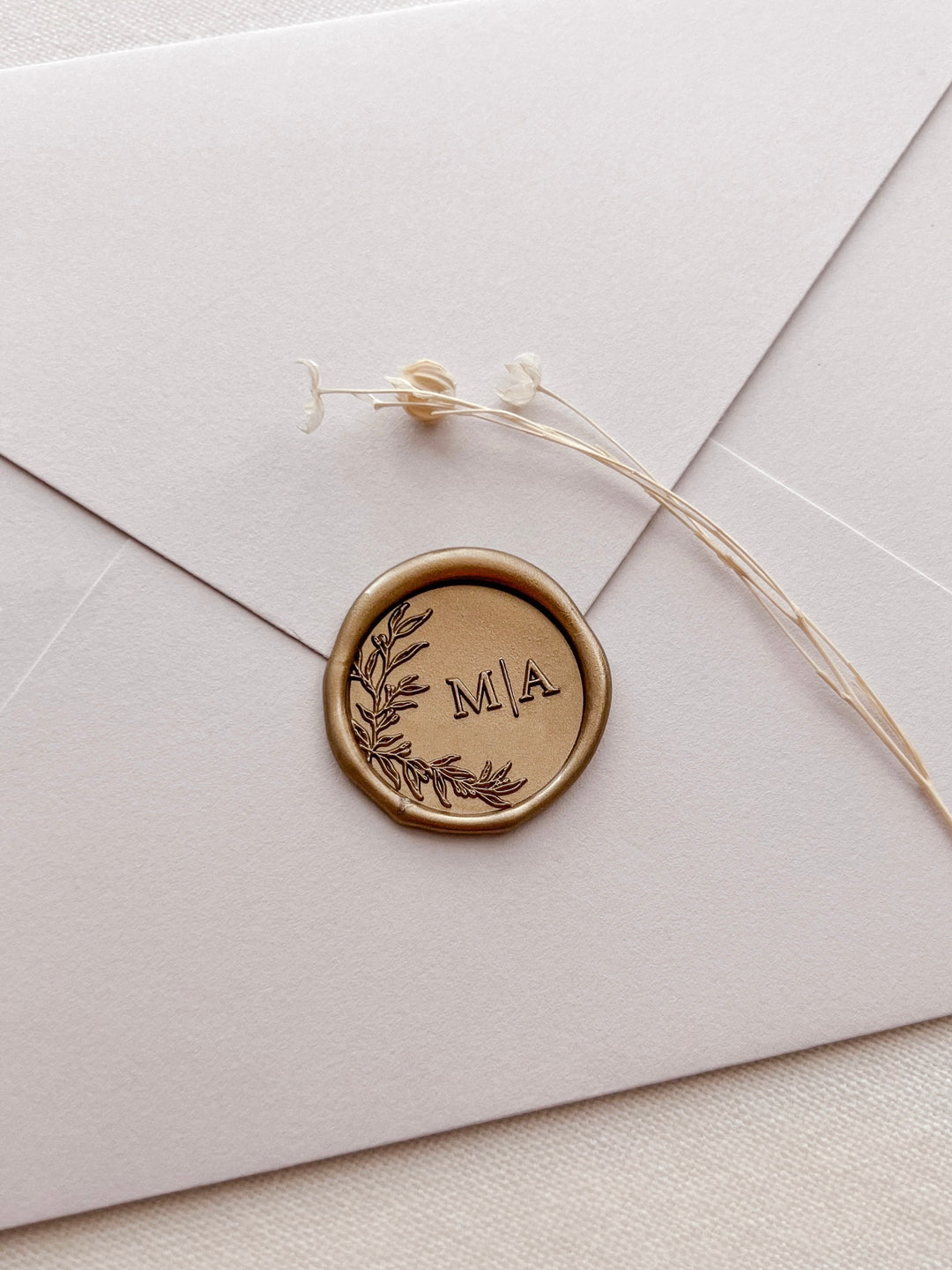 Gold botanical wreath custom monogram wax seal with personalized initials on a light beige envelope