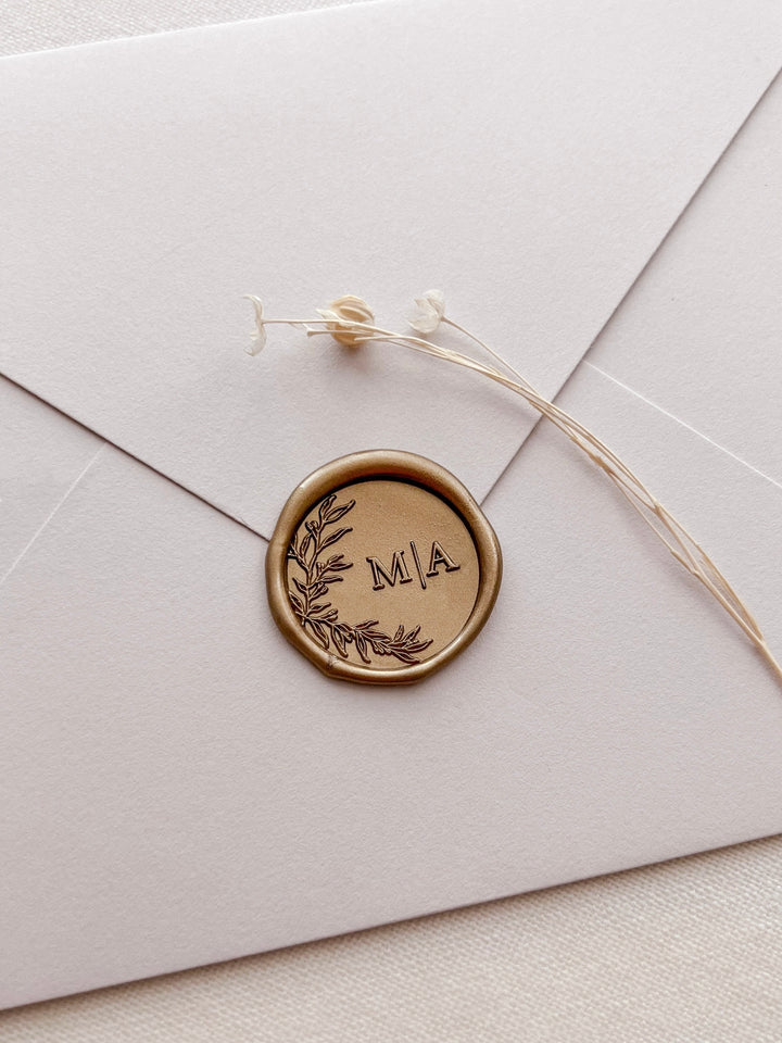 Gold botanical wreath custom monogram wax seal with personalized initials on a light beige envelope