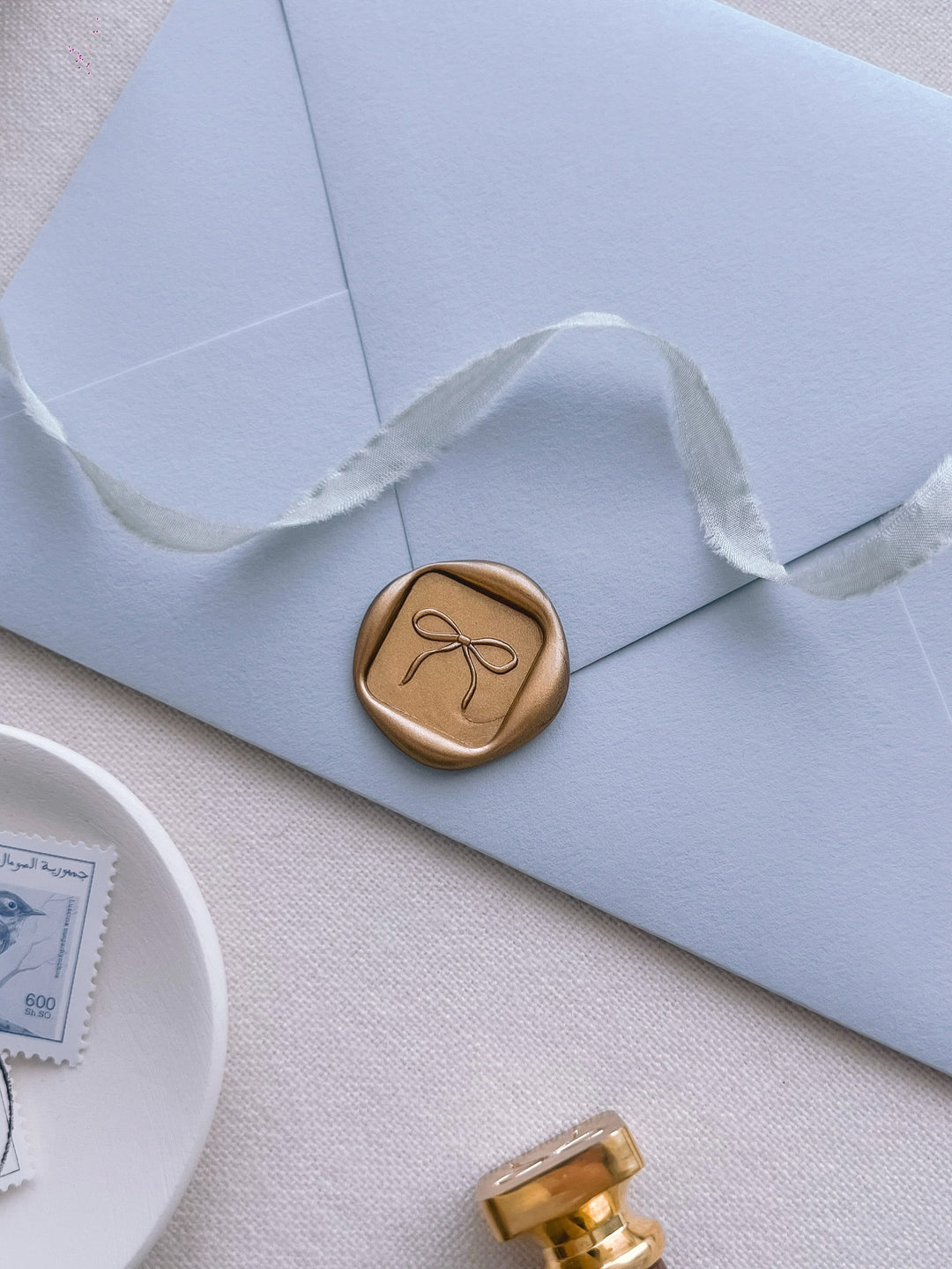 gold 3D bow mini square wax seal on a light blue envelope