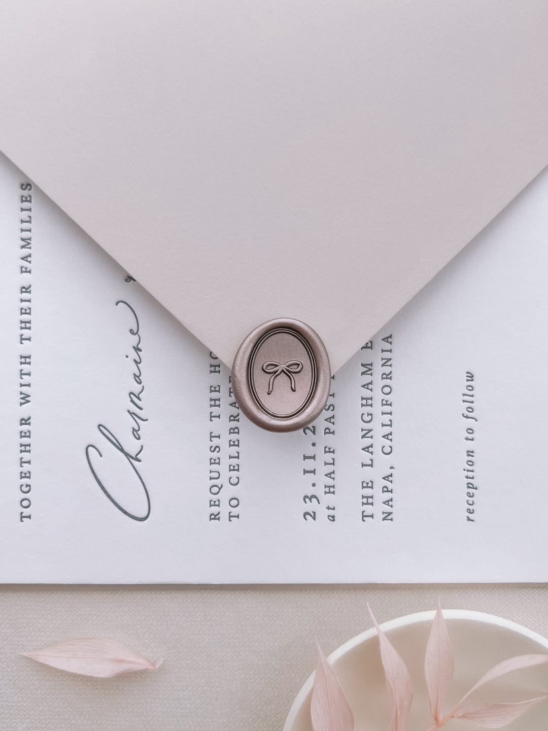 light bronze mini hand-drawn ribbon bow oval wax seal on a light grey envelope over a wedding invitation card