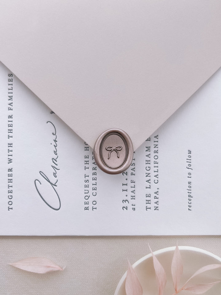 light bronze mini hand-drawn ribbon bow oval wax seal on a light grey envelope over a wedding invitation card