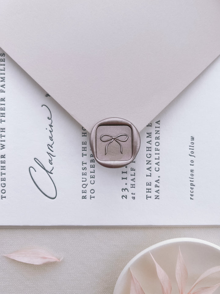 Light bronze 3D hand-drawn bow mini square wax seal on a white invitation card and light beige envelope 