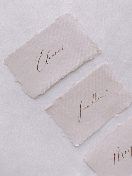 handmade paper place cards in light cream color hand lettered in modern calligraphy in brown ink_side angle