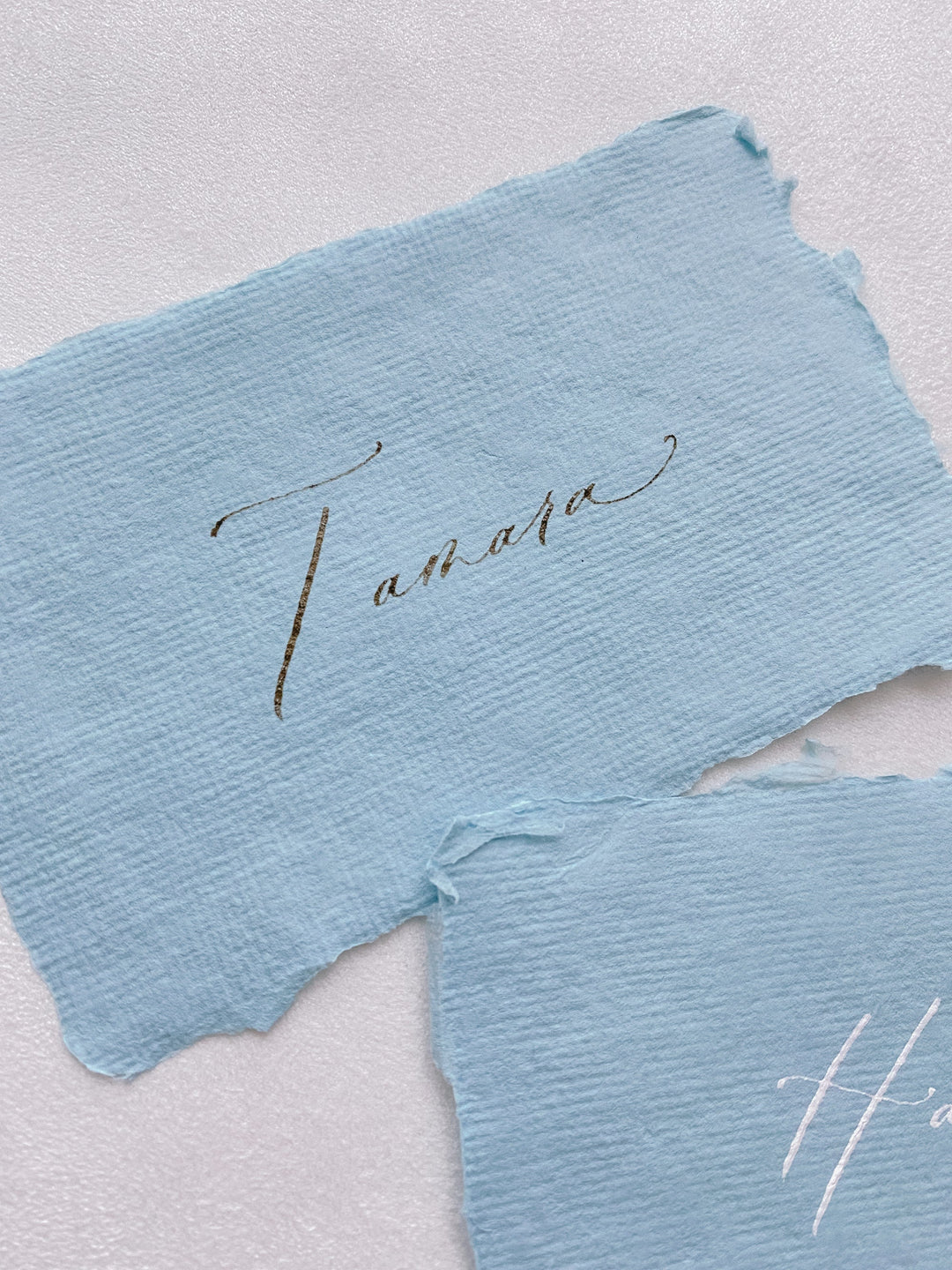 handmade paper place card in sky color hand lettered in modern calligraphy in brown ink_close angle