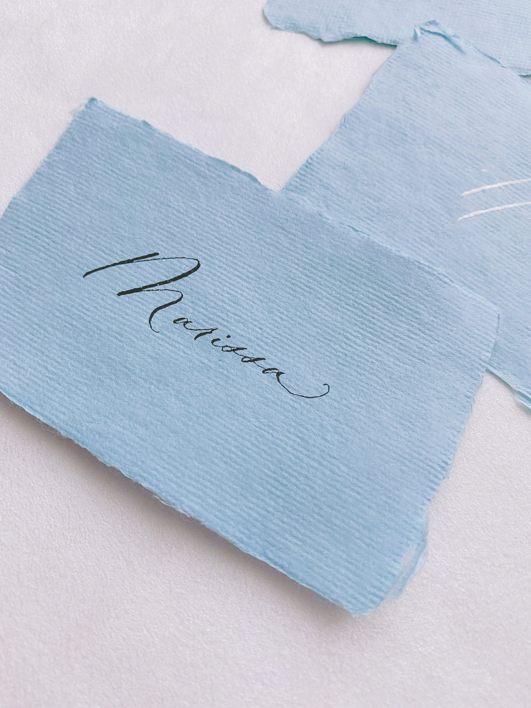 handmade paper place card in sky color hand lettered in modern calligraphy in black ink_side angle