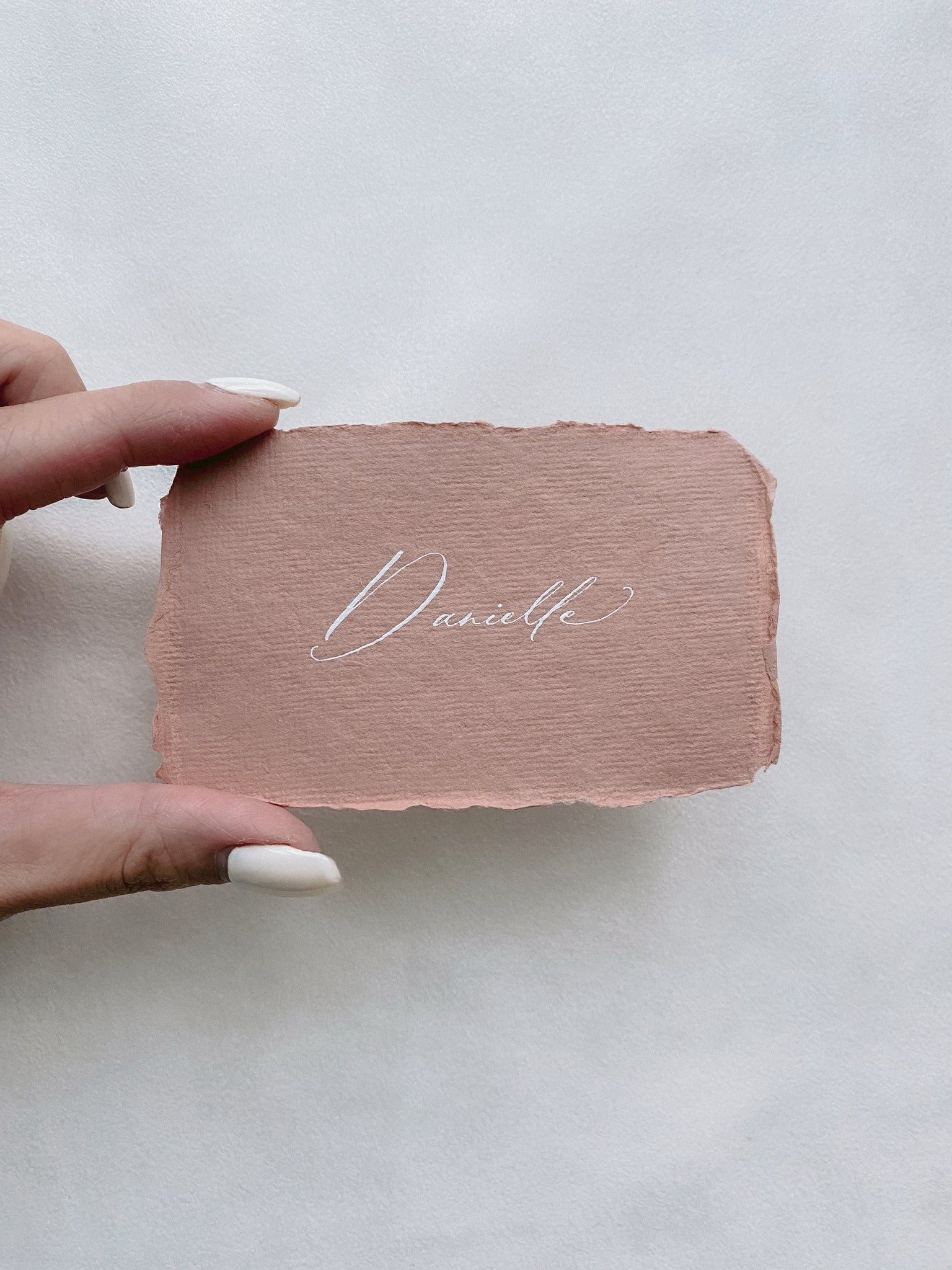 handmade paper place card in terracotta color hand lettered in modern calligraphy in white ink