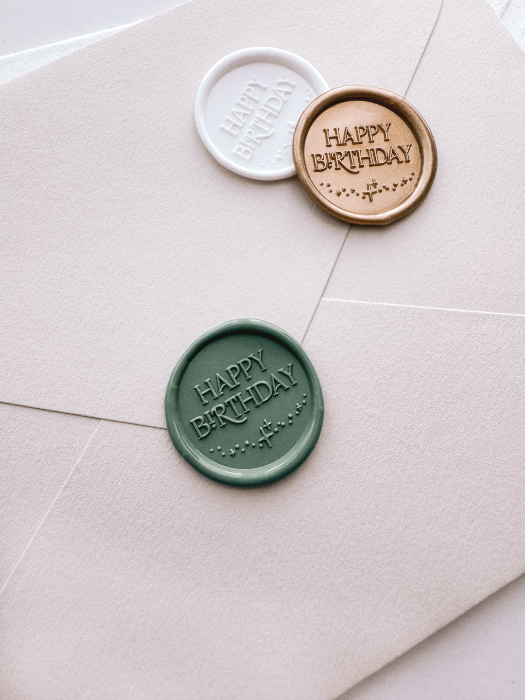 Sage green, gold, and white Happy Birthday wax seals on a light beige envelope