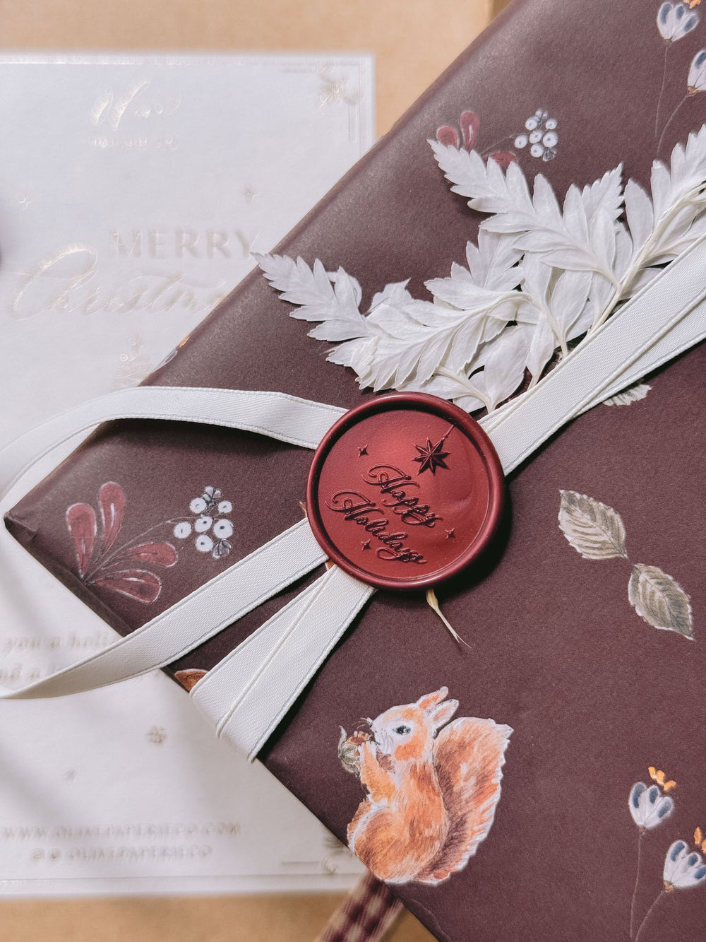 A dark metallic red wax seal that reads 'Happy Holidays' attached on a white decorative ribbon on a wrapped gift with brown festive wrapping paper