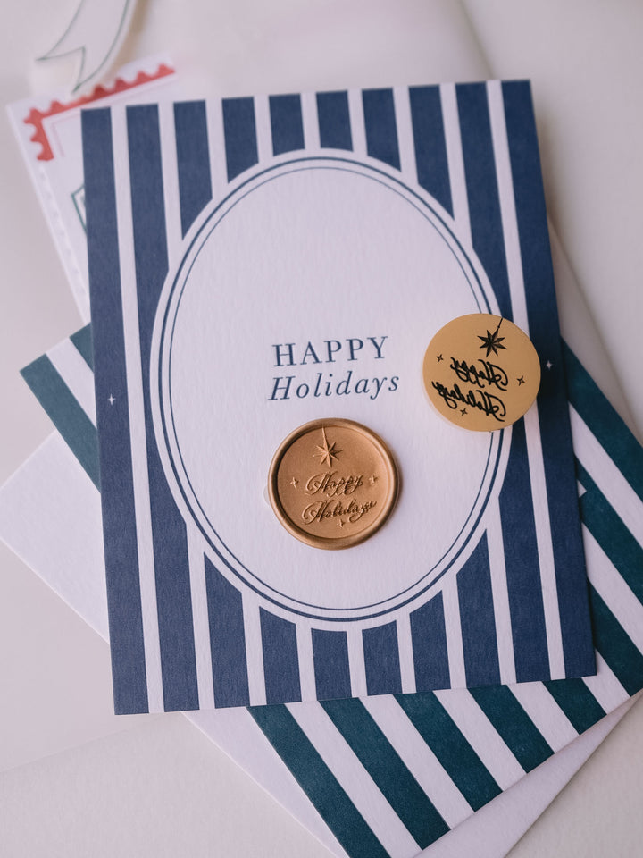 Gold Happy Holidays wax seal styled with a navy blue striped Christmas card with the greeting &