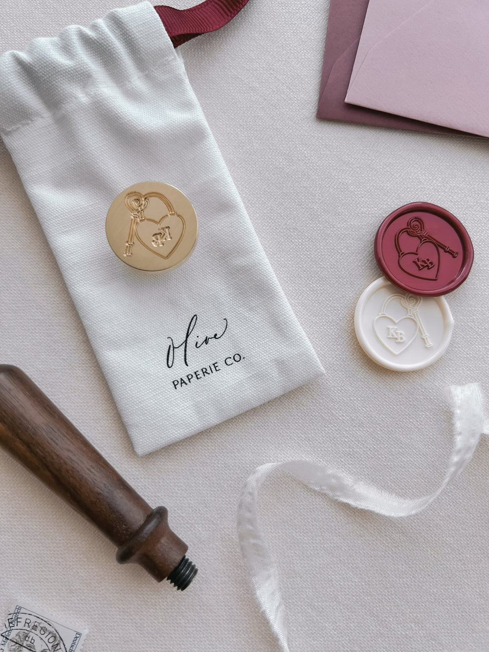 Custom initials heart padlock and key wax stamp head with off-white and metallic red heart lock wax seals and a walnut wood handle next to it