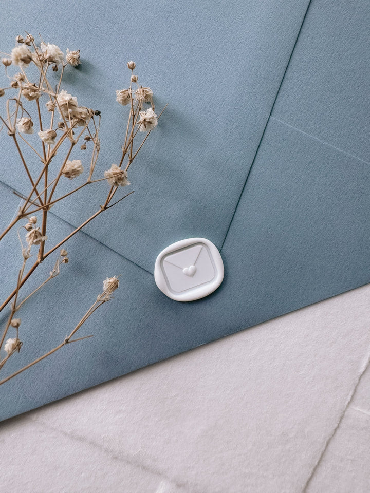 White mini heart sealed envelope wax seal on dusty blue envelope styled with dried flower branch