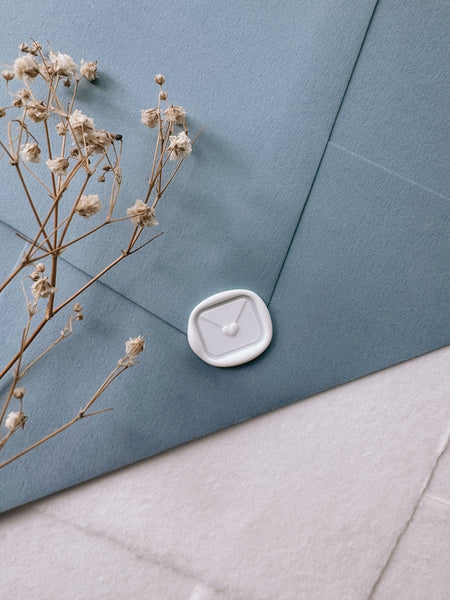 White mini heart sealed envelope wax seal on dusty blue envelope styled with dried flower branch