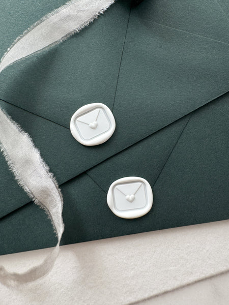 White mini heart sealed envelope wax seal on dark green envelopes styled with a strand of white silk ribbon
