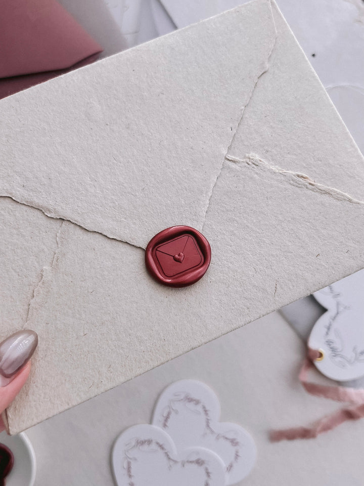 Dark metallic red 3D love letter wax seal on a light brown deckle-edge handmade paper envelope