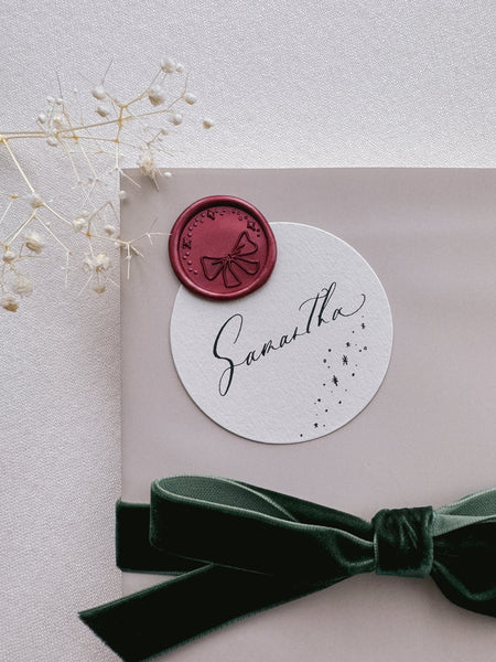 dark metallic red festive ribbon bow with stars design wax seal on a wrapped Christmas gift with name tag