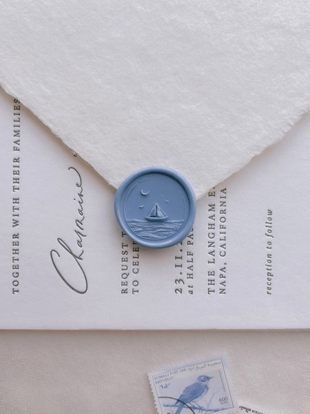 Blue nautical themed wax seal featuring a sailboat over ocean waves with a crescent moon on white invitation card and envelope