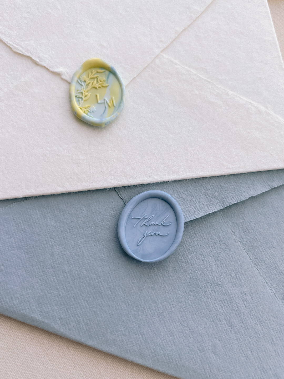 A yellow and blue mixed color monogram wax seal and a mixed blue colored thank you oval wax seal 