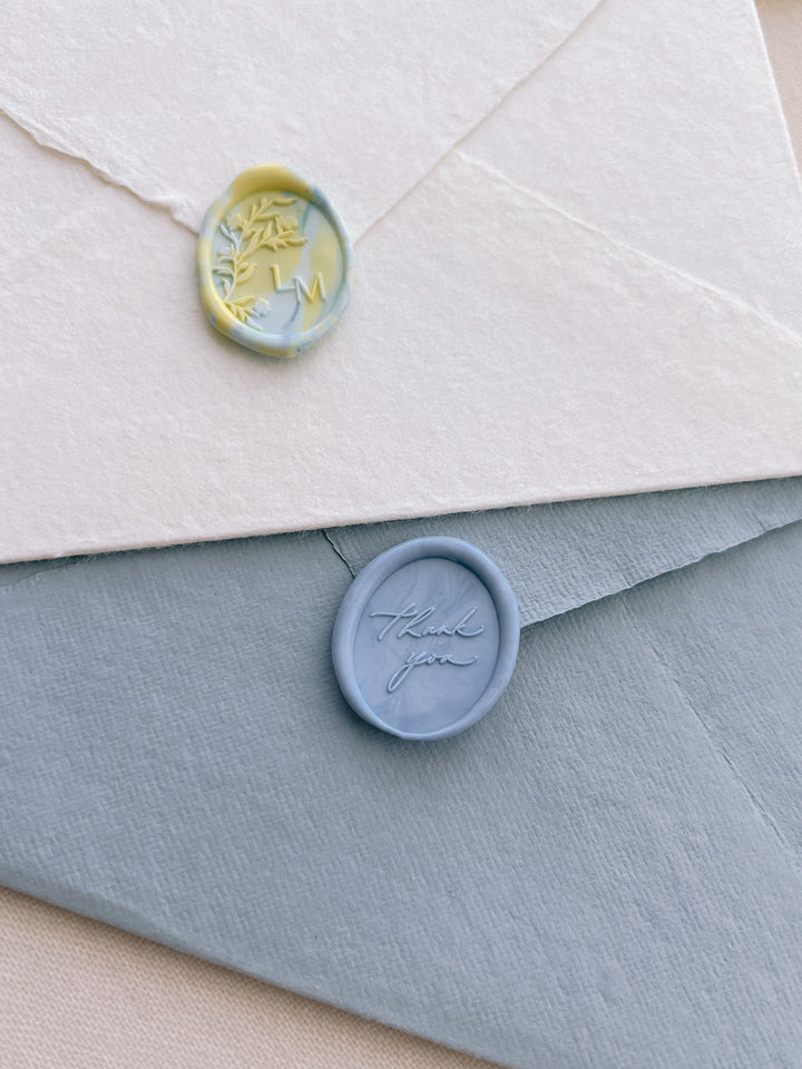 A yellow and blue mixed color monogram wax seal and a mixed blue colored thank you oval wax seal 