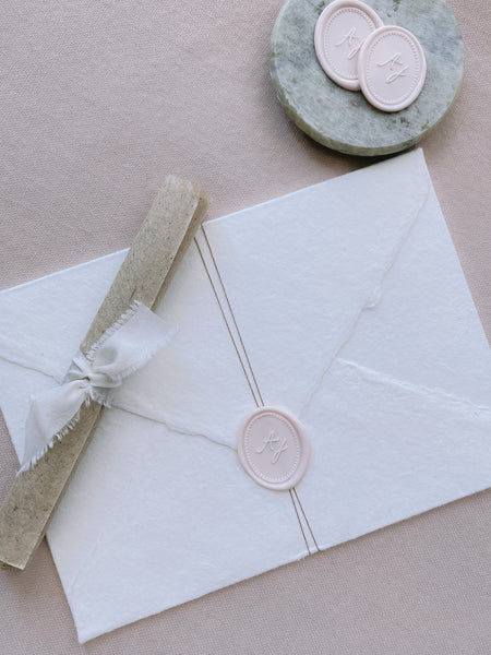 Oval monogram custom wax seal in ivory nude color on white handmade paper envelope wrapped with fine twine styled with a small gray stone dish with ivory nude color wax seals