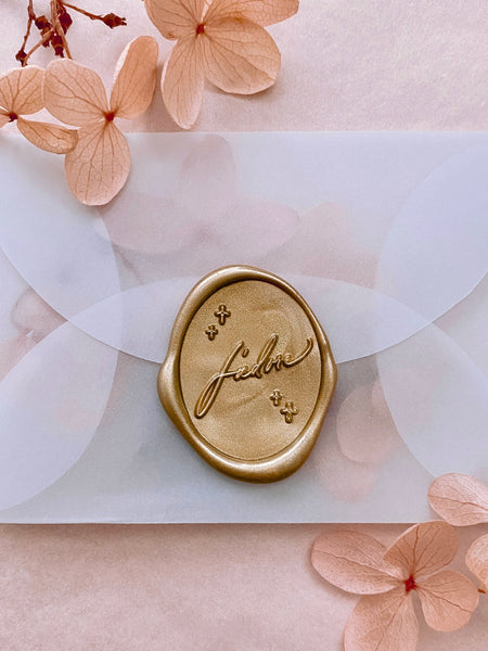Gold J'adore oval wax seal on mini vellum envelope styled with blush dried hydrangea petals