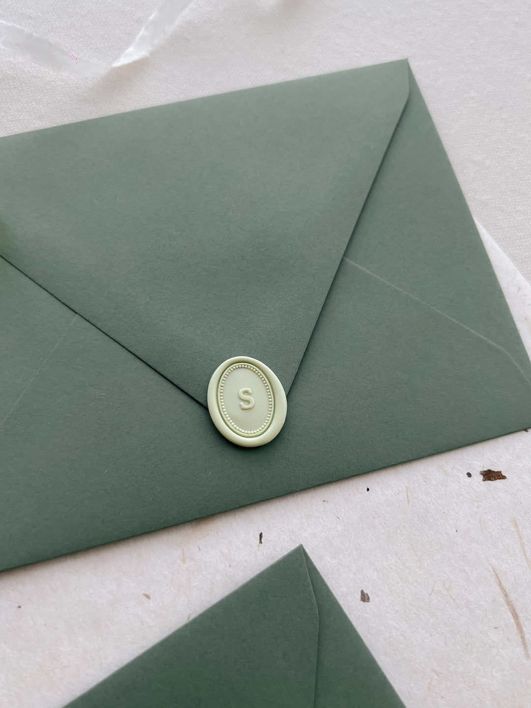 Pale green personalized alphabet mini oval wax seal on an olive green envelope