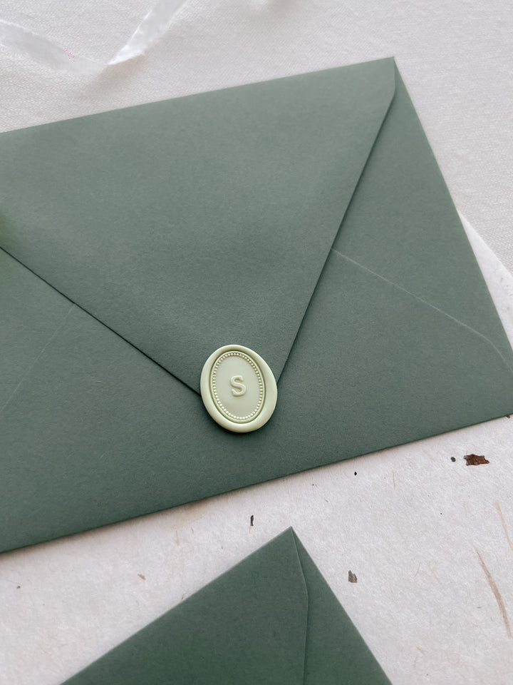 Pale green personalized alphabet mini oval wax seal on an olive green envelope