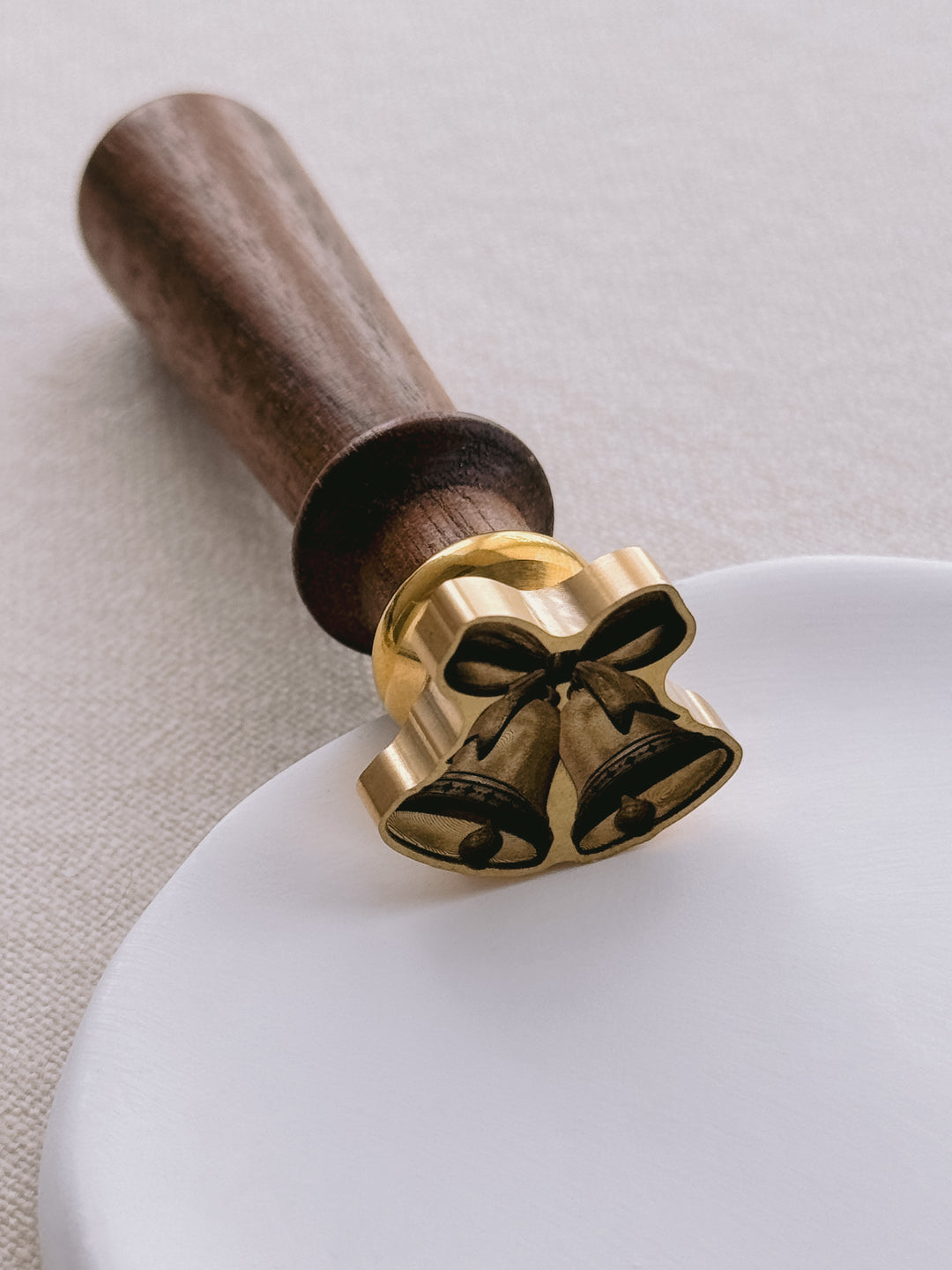 Close-up of a 3D die-cut wax seal stamp with a walnut wooden handle, wax seal design featuring two jingle bells tied with a ribbon bow