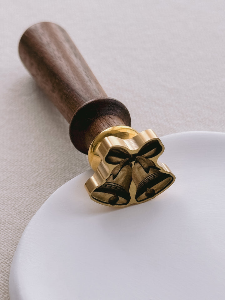 Close-up of a 3D die-cut wax seal stamp with a walnut wooden handle, wax seal design featuring two jingle bells tied with a ribbon bow