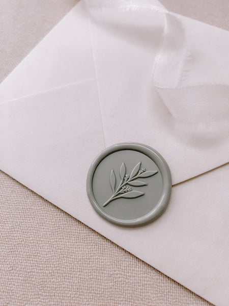 Sage green leaf branch wax seal in sage green on white paper envelope with white silk ribbon