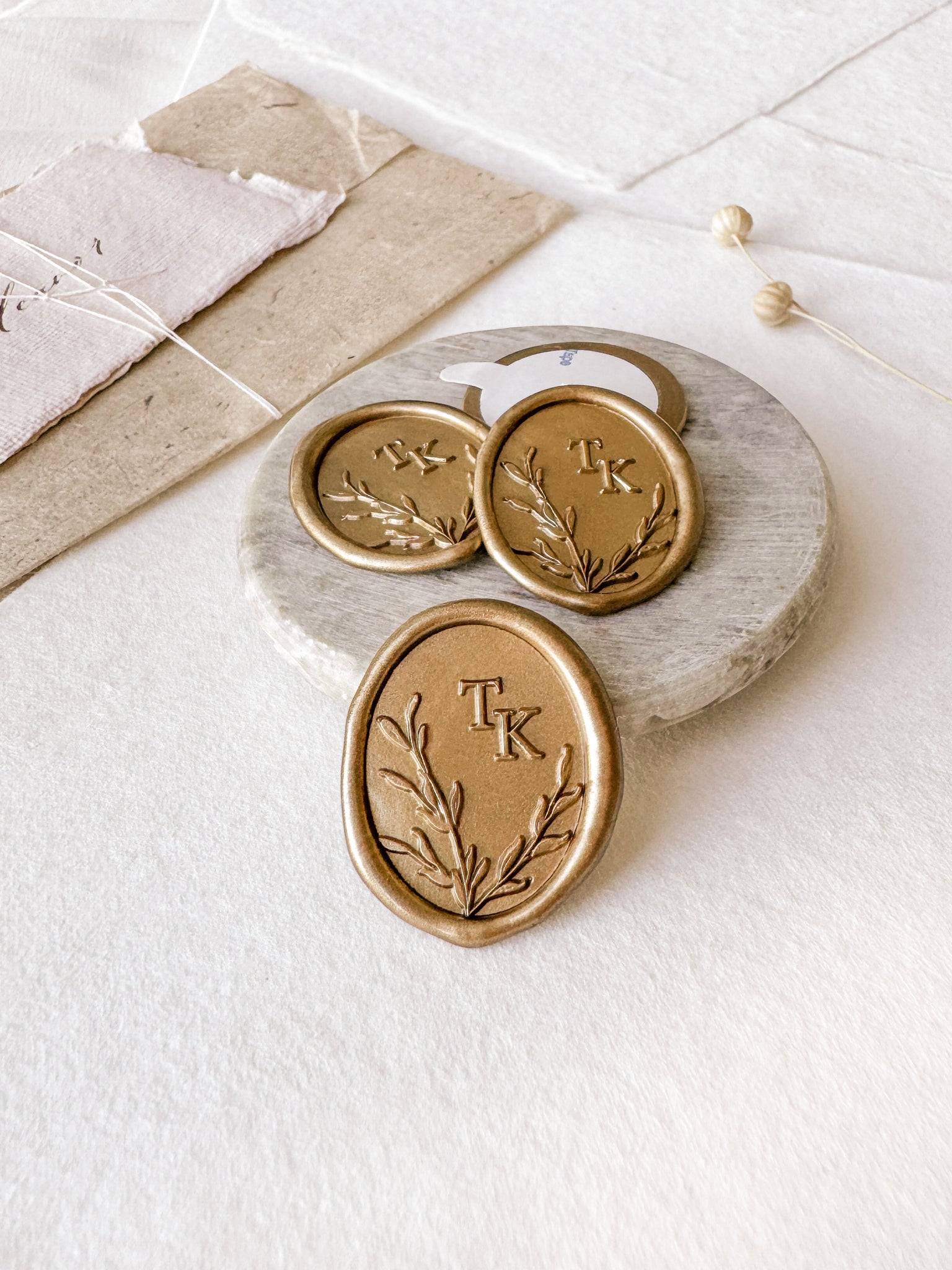Leaves wreath monogram oval custom wax seals in gold  styled with a small gray stone dish, handmade paper and a dried floral branch