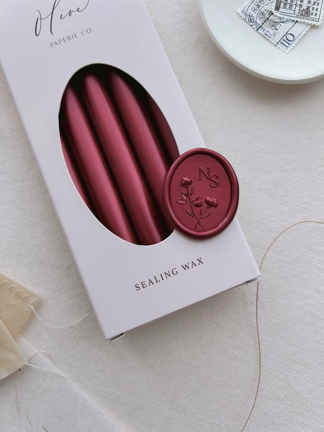 Dark metallic red custom floral monogram wax seal with personalized initials on a box of metallic red sealing wax sticks