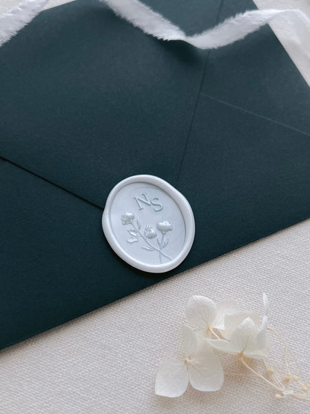Pearl white 3D flower design personalized initials wax seal on a dark green wedding invitation envelope