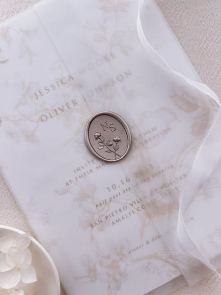 Light bronze floral monogram oval wax seal with personalized initials on a wedding invitation suite wrapped in a printed floral vellum jacket