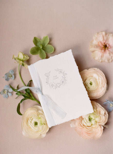 Her letterpress floral wreath vow book with soft white colored silk ribbon styled with flowers