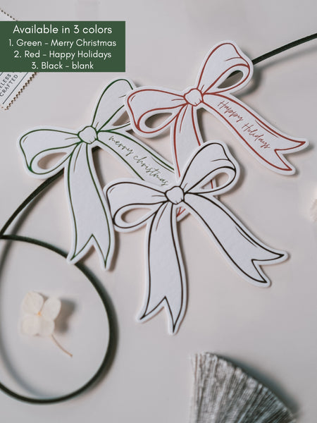 Festive die-cut bow gift tags in green, red and black with text Merry Christmas and Happy Holidays 