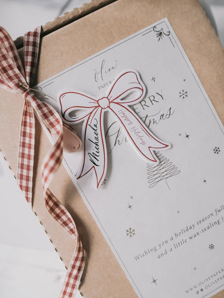 Festive bow shaped red gift tag personalized with name on a wrapped Christmas gift