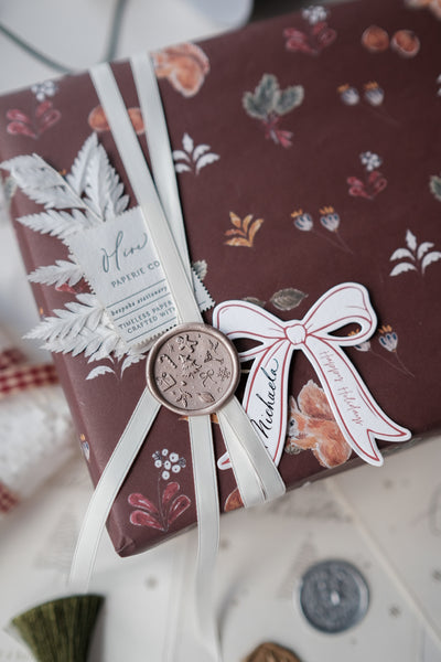 Die-cut bow gift tag on a wrapped Christmas gift decorated with a festive holiday wax seal