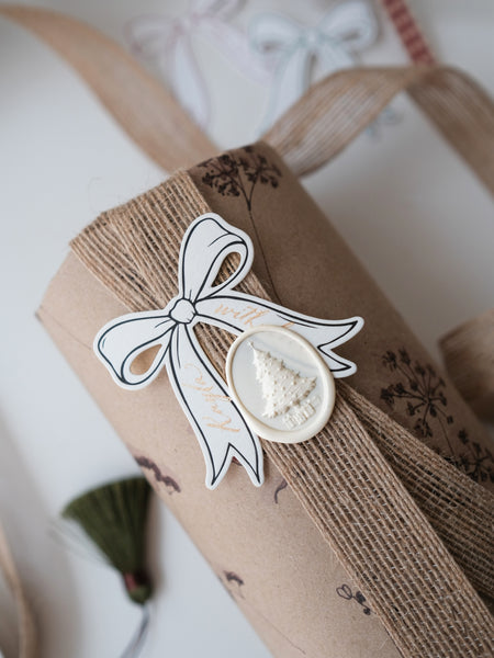 Die-cut bow gift tag on a wrapped Christmas gift decorated with a white 3D Christmas tree wax seal