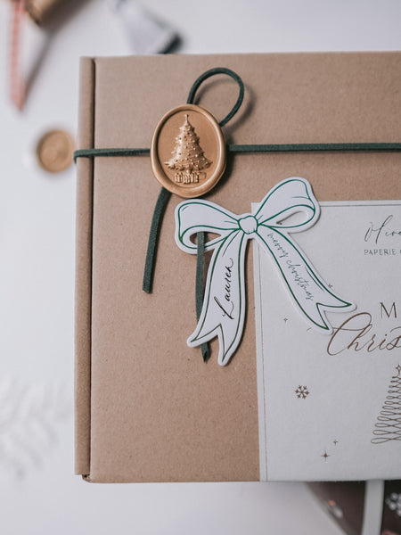 Die-cut bow green name tag on a wrapped Christmas gift decorated with a gold 3D Christmas tree wax seal