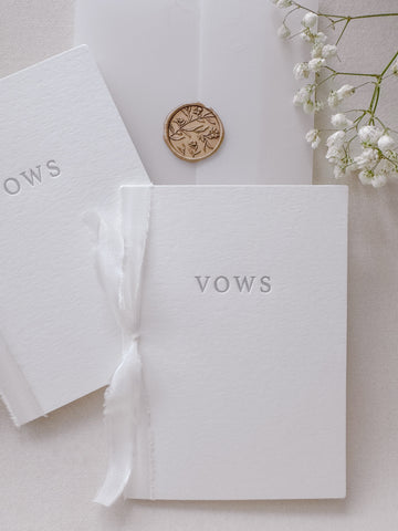 Set of two wedding vow book with VOWS letterpress embossed in gray ink, tied in white silk ribbon and styled with vellum jacket, a gold floral wax seal and a white floral branch