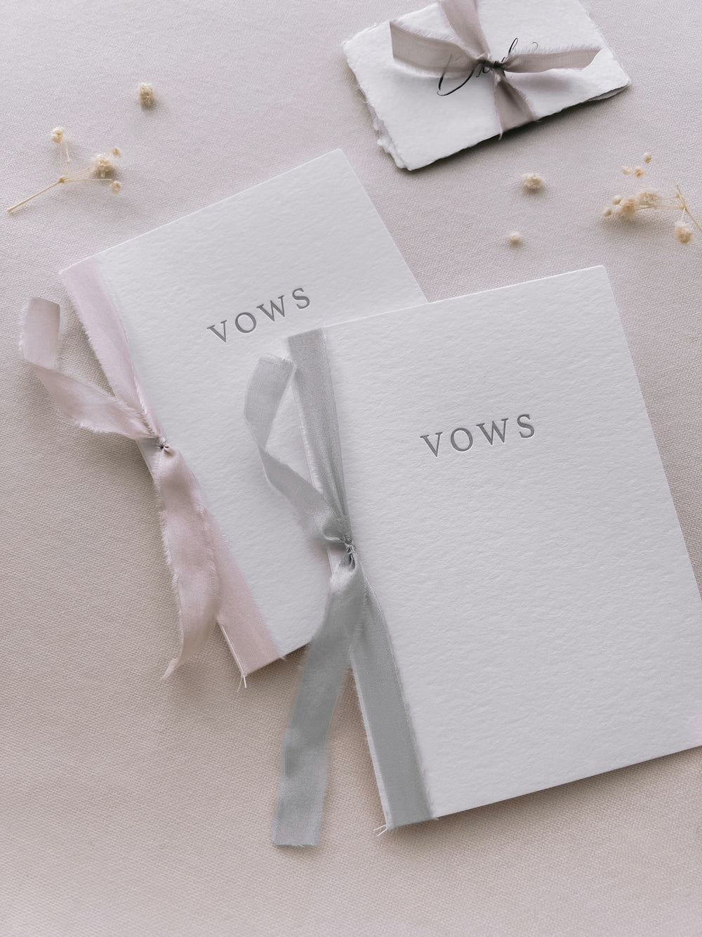 white letterpress vow books tied in pink and gray silk ribbons