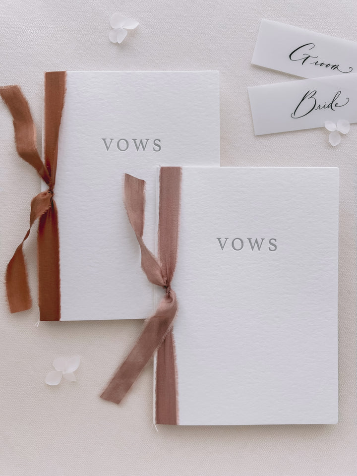 white letterpress vow books tied in cinnamon and rose colored silk ribbons